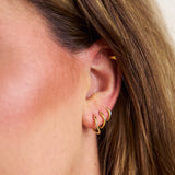 Close-up of a person wearing gold hoop earrings with a blurred background