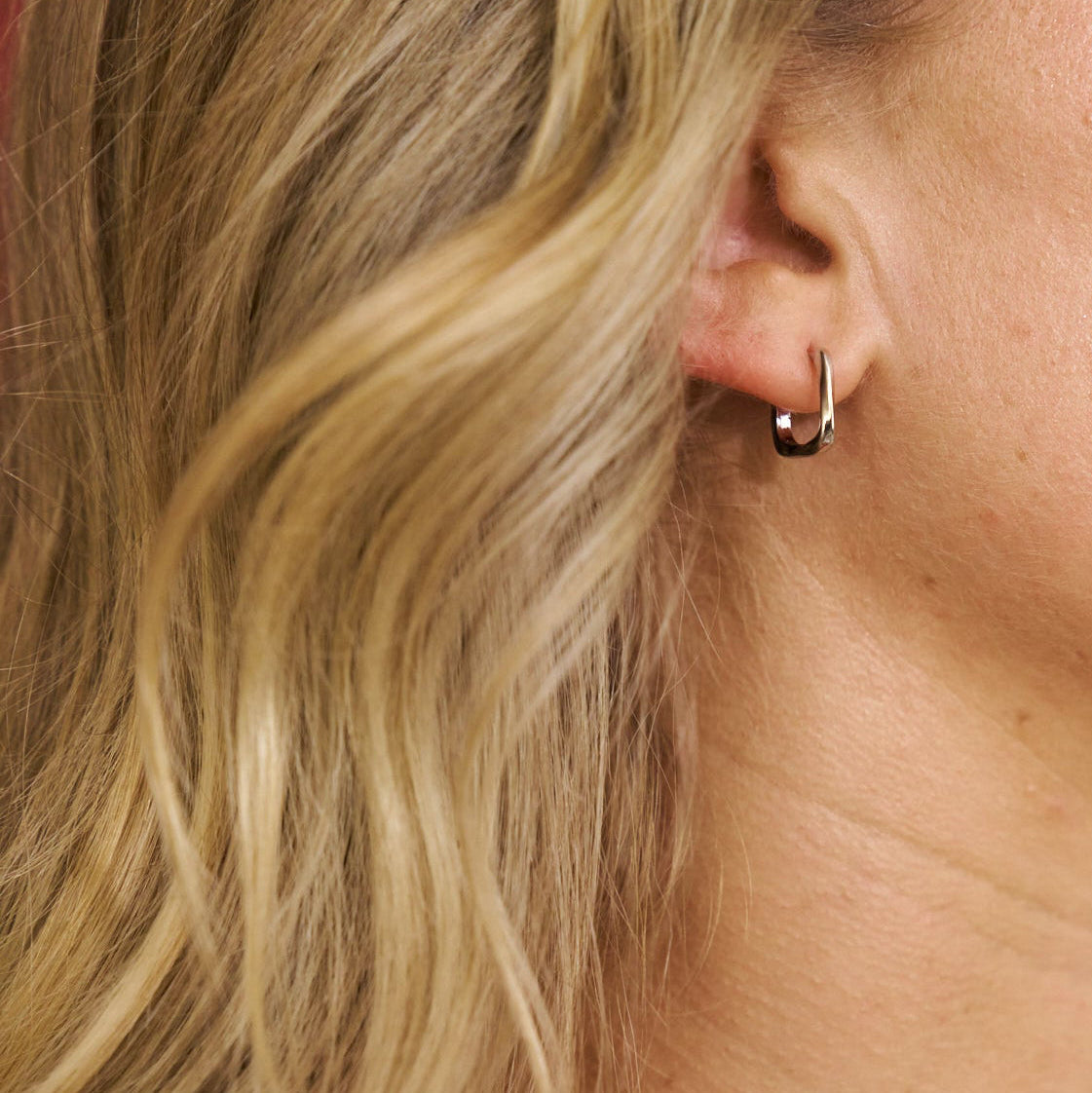 Close-up of an ear wearing a small hoop earring with blonde hair.