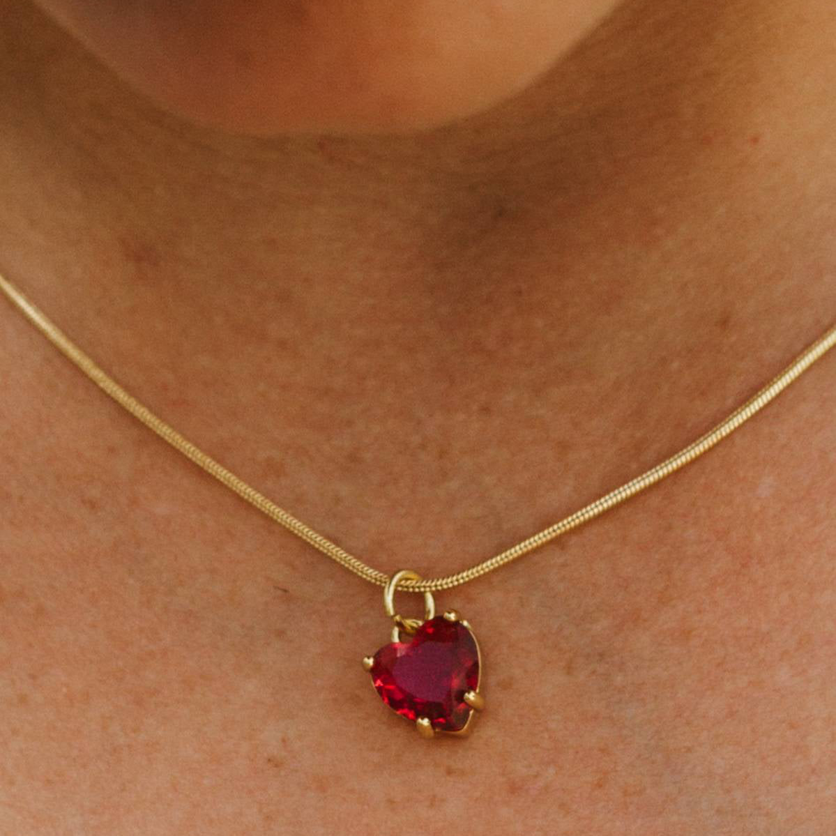 Gold necklace with a red heart-shaped pendant on a person's neck.