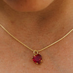 Gold necklace with a red heart-shaped pendant on a person's neck.
