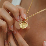 Gold necklace with a pendant held by hands against a neutral background