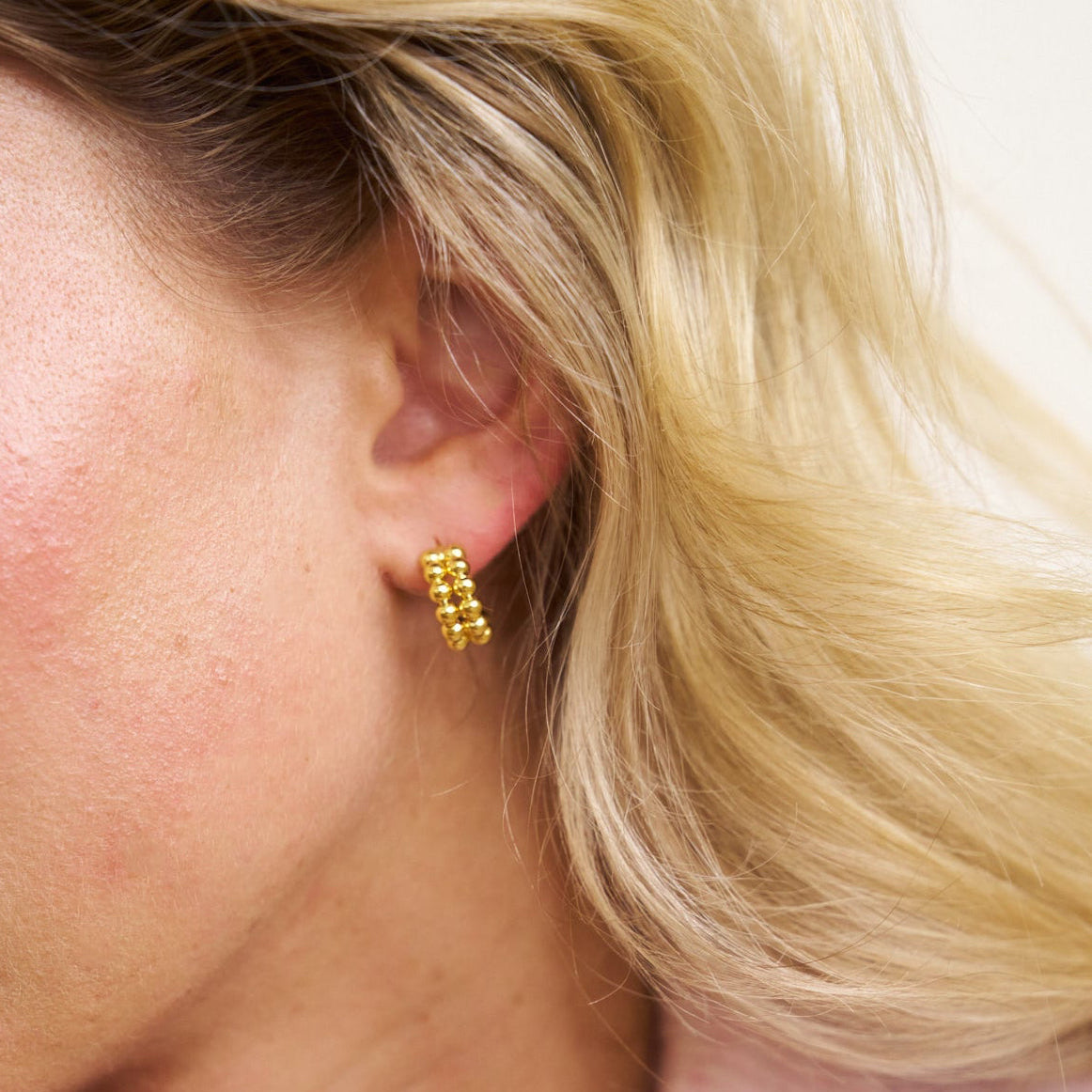 Close-up of a person wearing gold hoop earrings with blonde hair.