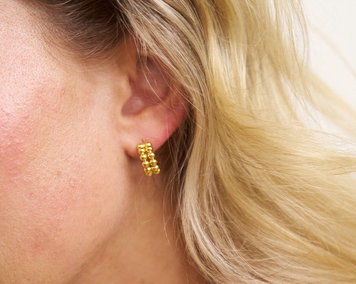 Close-up of a person wearing gold hoop earrings with blonde hair.
