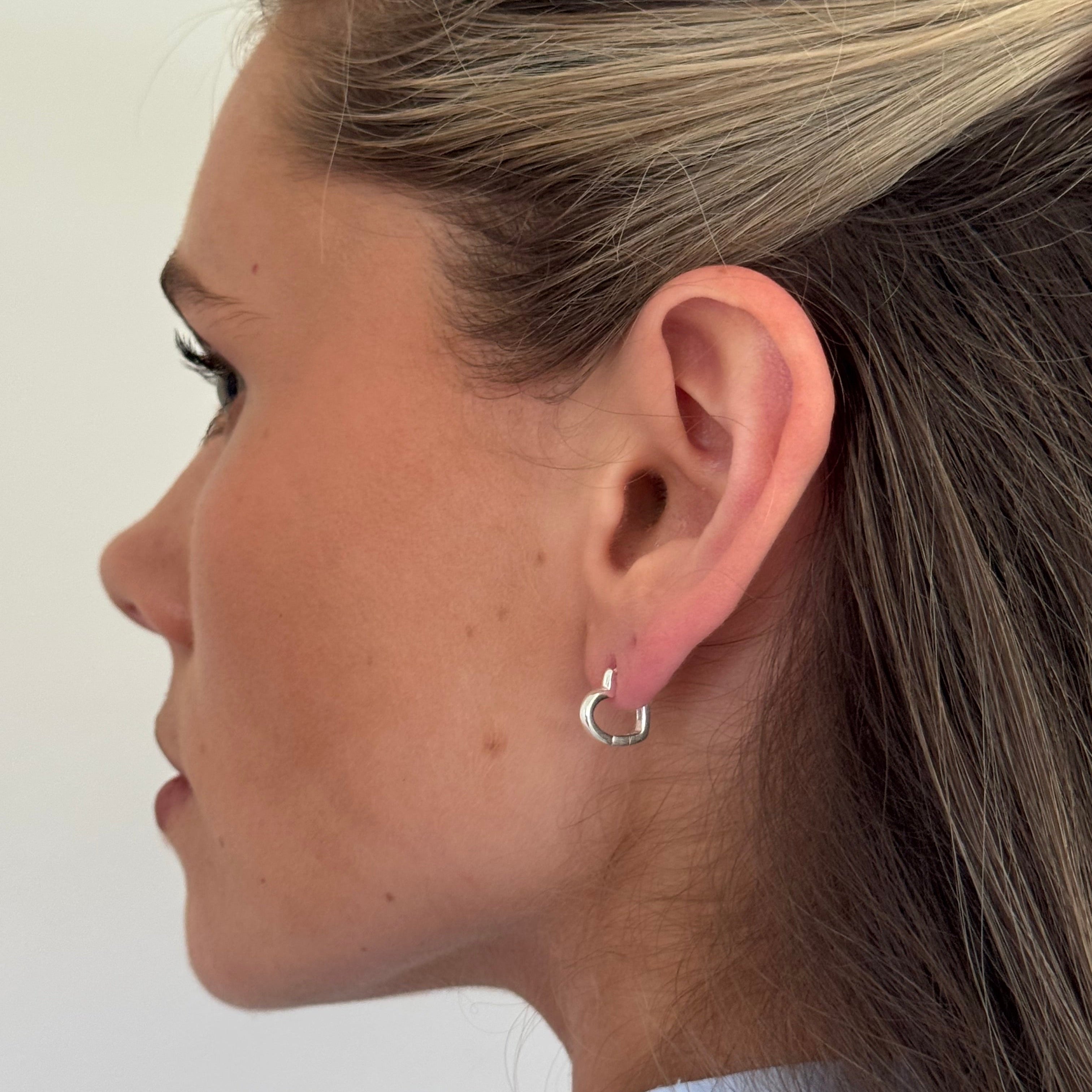 Close-up of a person wearing a silver hoop earring on a plain background