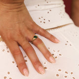 Hand wearing a gold ring with a green gemstone on a white lace fabric background