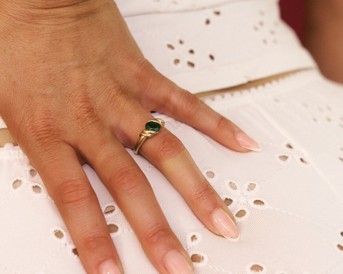 Hand wearing a gold ring with a green gemstone on a white lace fabric background