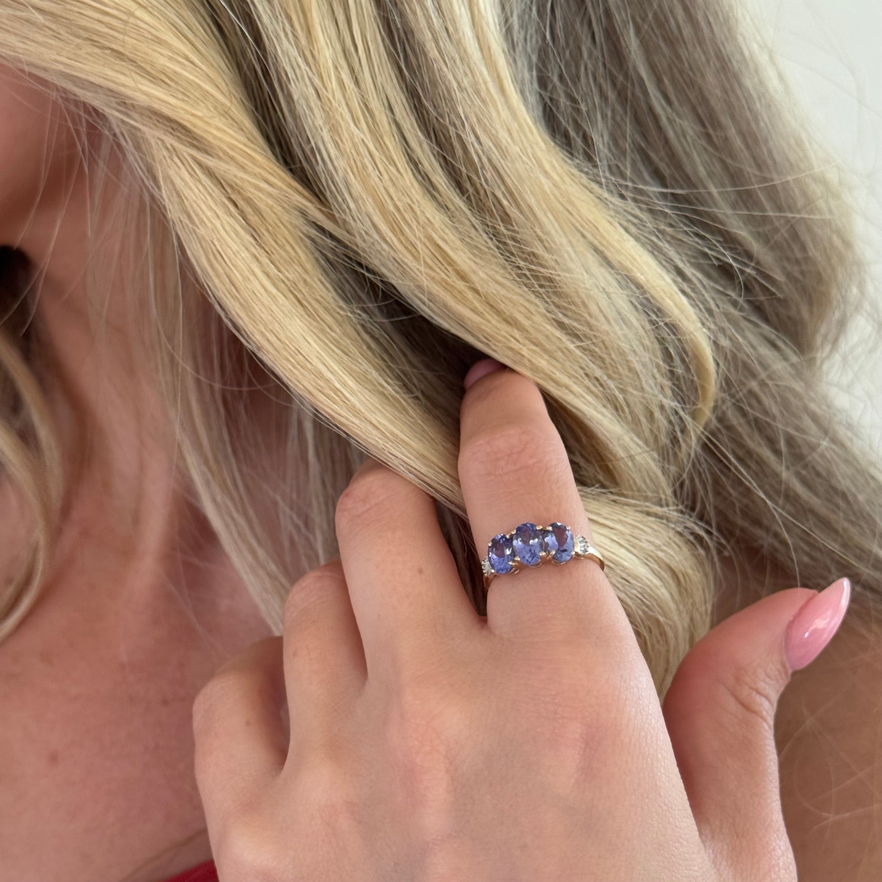 Close-up of a hand with a ring featuring a blue gemstone, touching blonde hair.