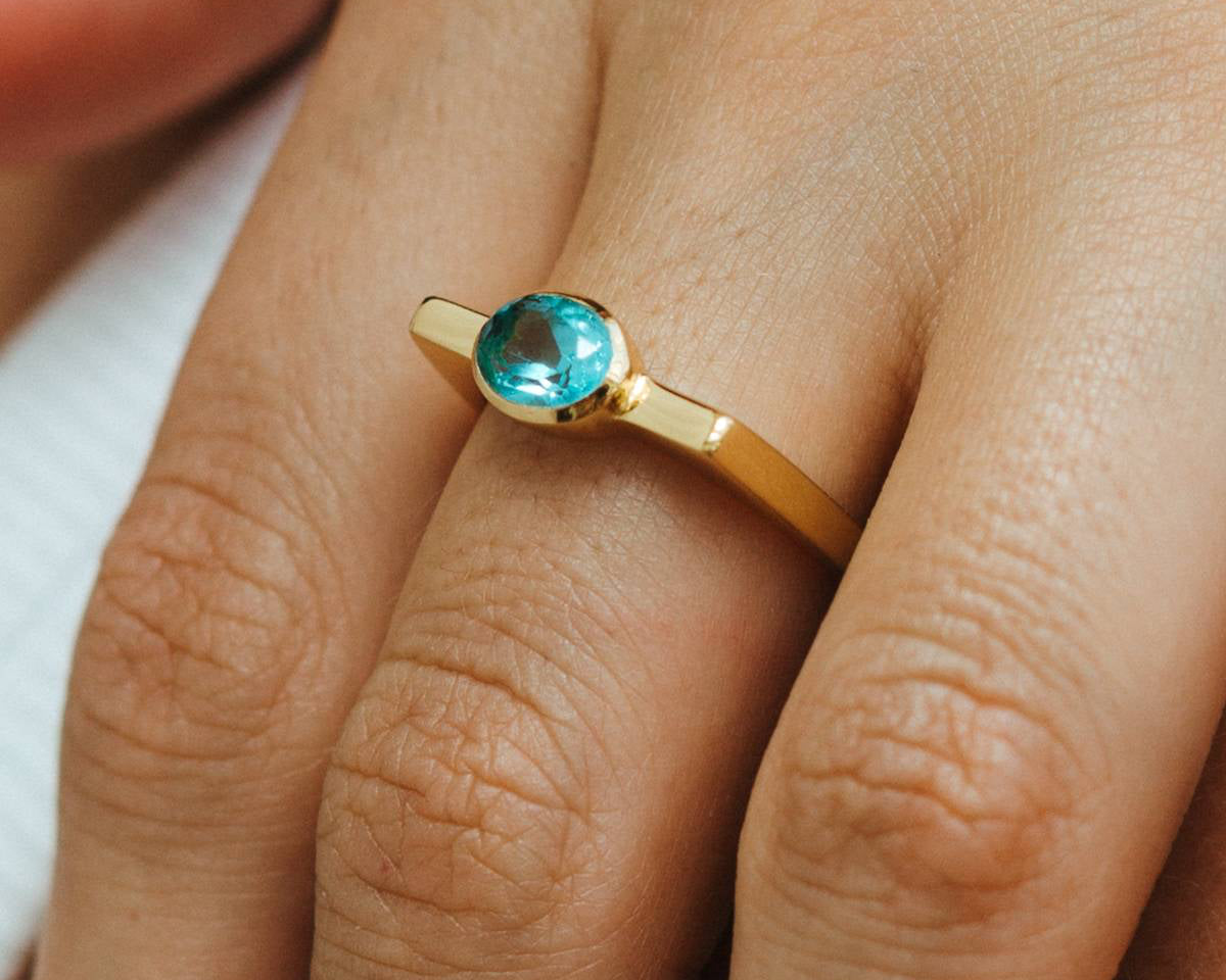 Gold ring with a blue gemstone on a person's finger