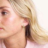 Close-up of a woman wearing a green hoop earring with a plain background