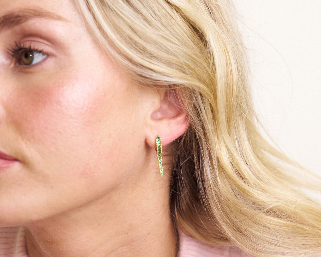 Close-up of a woman wearing a green hoop earring with a plain background