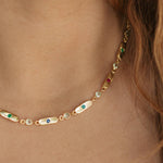 A close-up of a gold chain necklace worn on a model's neck, featuring elongated white onyx-like beads with small green and blue inlays, and clear faceted beads.