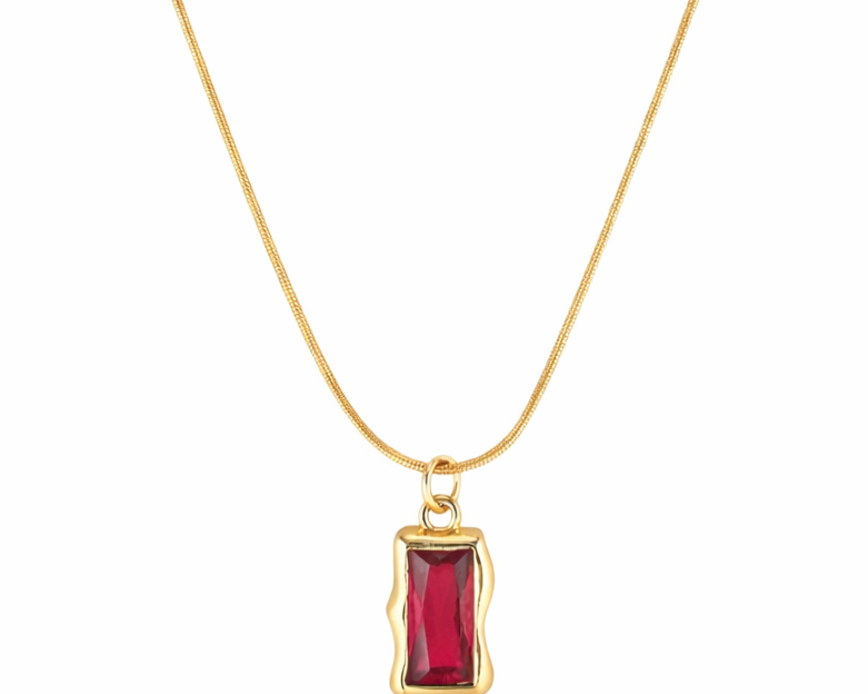 Gold necklace with a red gemstone pendant on a white background