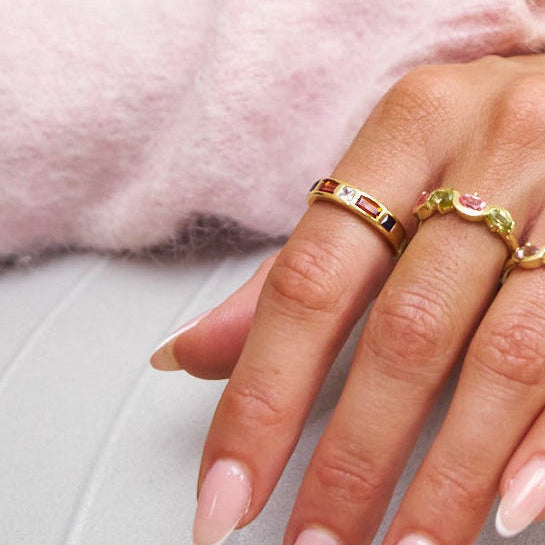 Close-up of a hand wearing gold rings with a soft pink background