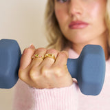 Person holding a blue dumbbell with close-up of hands and rings.
