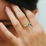 Close-up of a hand wearing a gold ring with a blue gemstone, blurred background