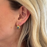 Close-up of an ear wearing a gold earring with a green gemstone.