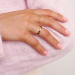 Hand wearing a gold ring on a pink textured background