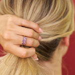 Close-up of a hand with a pink ring holding hair, against a blurred background
