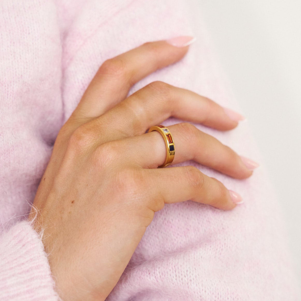 Hand wearing a gold ring on a pink textured background