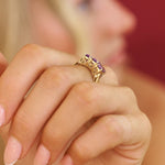 Gold ring with purple gemstones on a person's finger against a blurred background