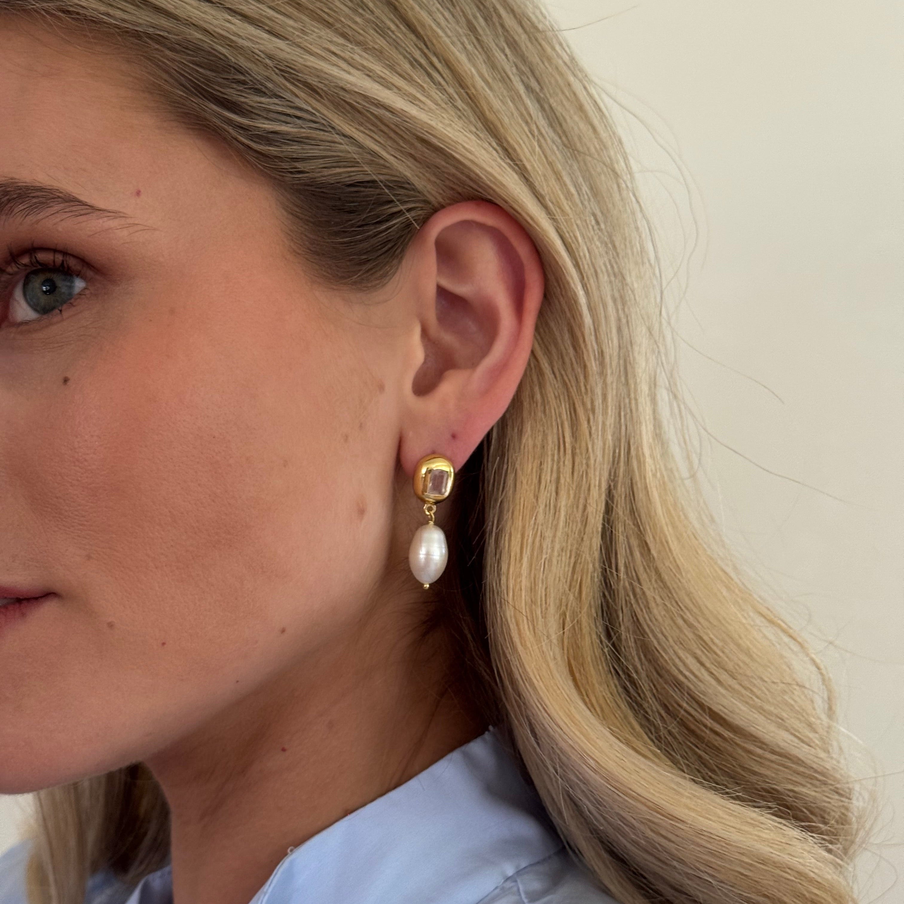 Close-up of a person wearing pearl earrings with a neutral background