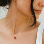 Close-up of a woman wearing a gold necklace with a red pendant and gold earrings.