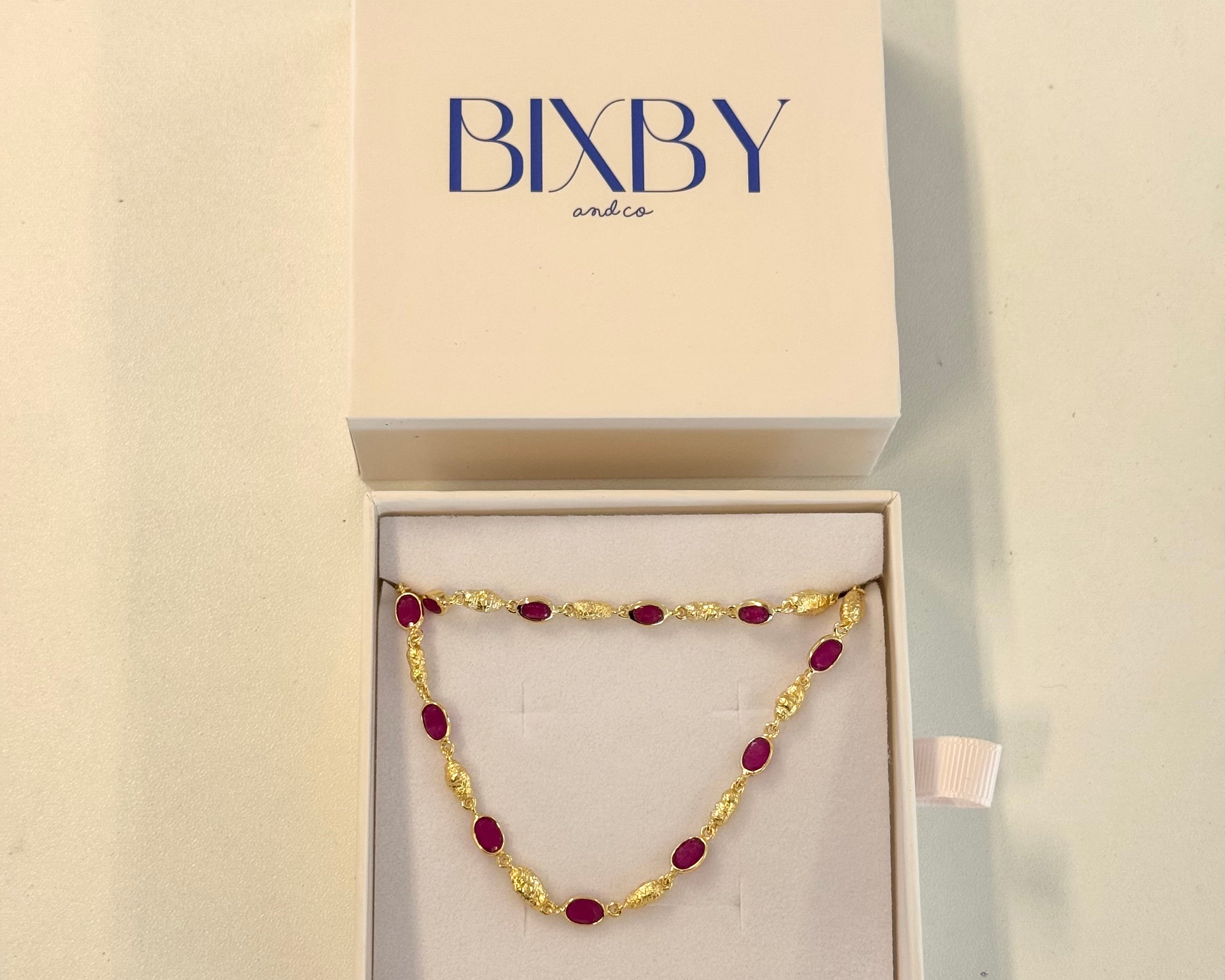 Gold and red beaded necklace in a Bixby box on a beige background