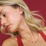 Woman wearing a gold and red beaded necklace and earrings against a red background