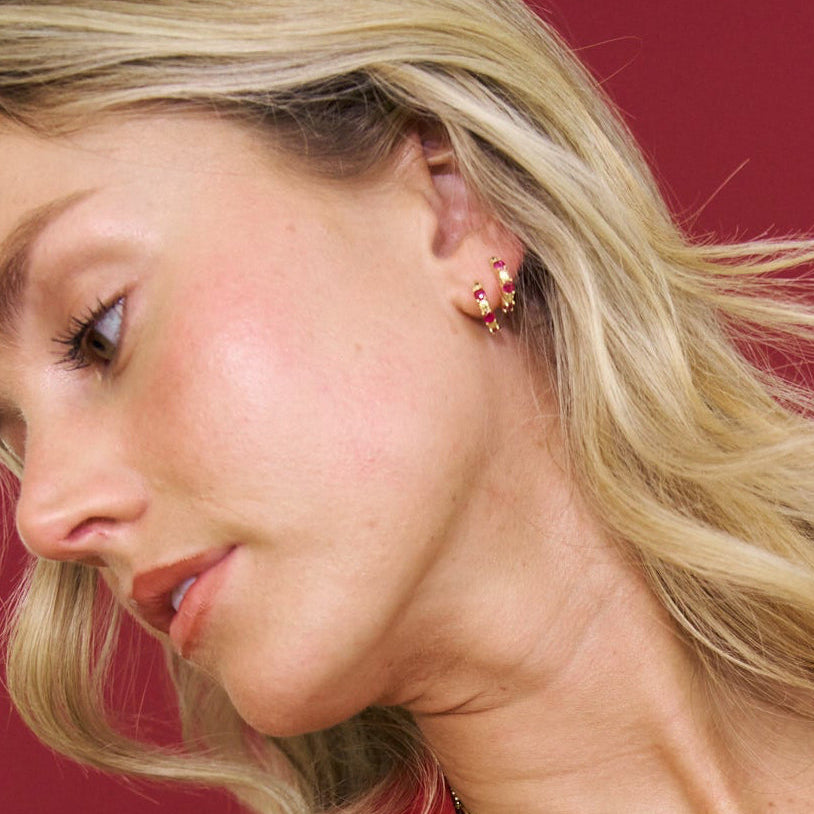 Woman wearing a gold and red beaded necklace and earrings against a red background