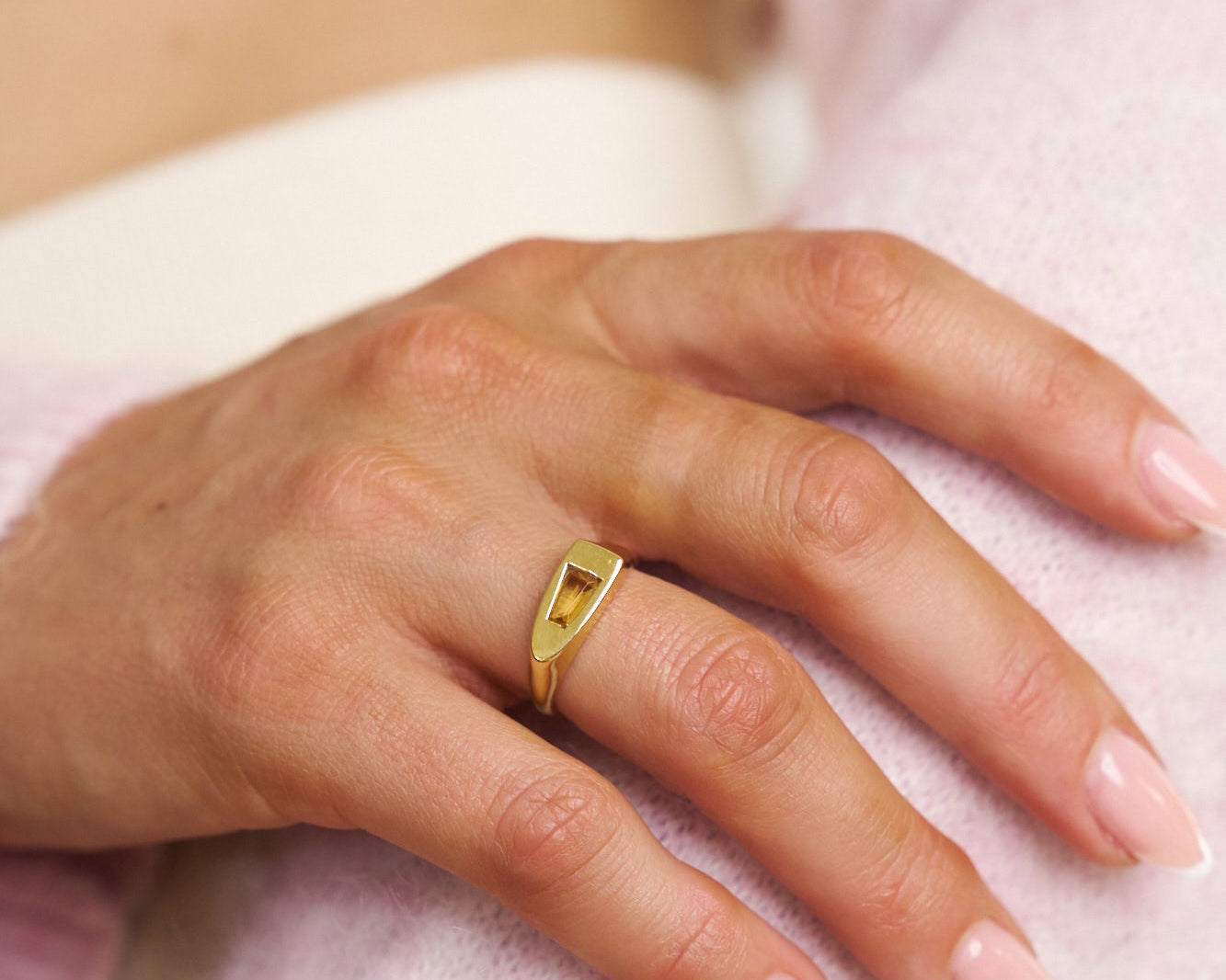 Hand wearing a gold ring on a soft pink background