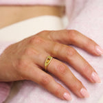 Hand wearing a gold ring on a soft pink background