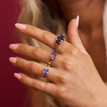 Close-up of a hand wearing a ring with purple gemstones against a blurred background