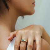 Close-up of a hand wearing a gold ring with a green gemstone, resting on a shoulder.
