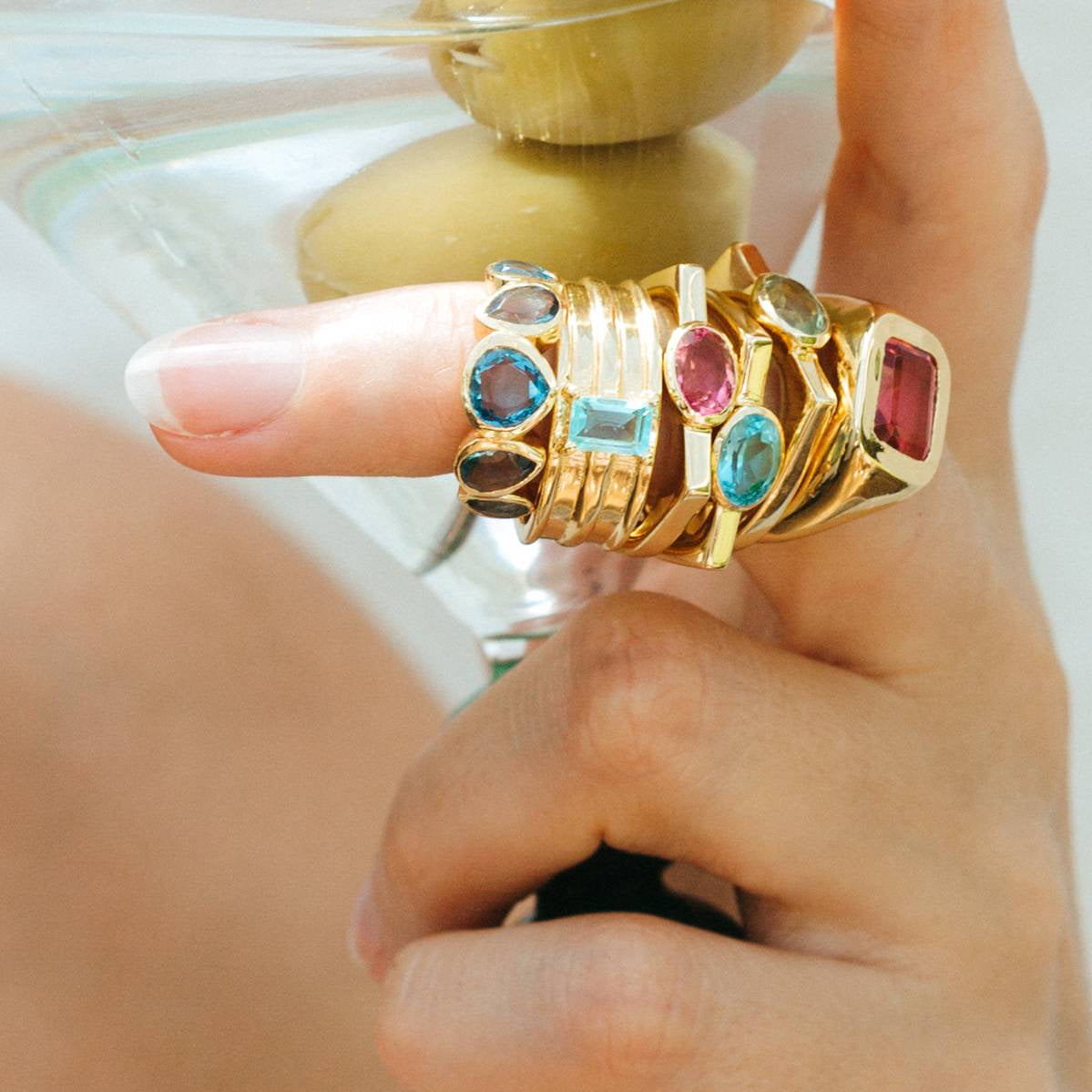 Hand wearing multiple gold rings with gemstones on a blurred background