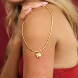 Gold necklace with a heart pendant worn by a person against a red background