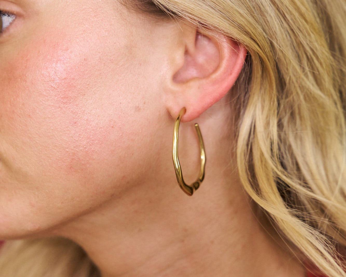 Close-up of a person wearing a gold hoop earring with a blurred background