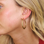 Close-up of a person wearing a gold hoop earring with a blurred background