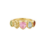 A gold ring featuring five heart-shaped gemstones in different colors: light green, pale yellow, pink, light blue, and dark red, set in a polished gold band on a light beige background.