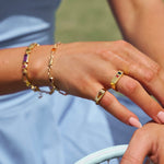 Close-up of hands wearing gold rings and bracelets with a blurred background