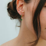 Close-up of a person wearing green earrings with a neutral background