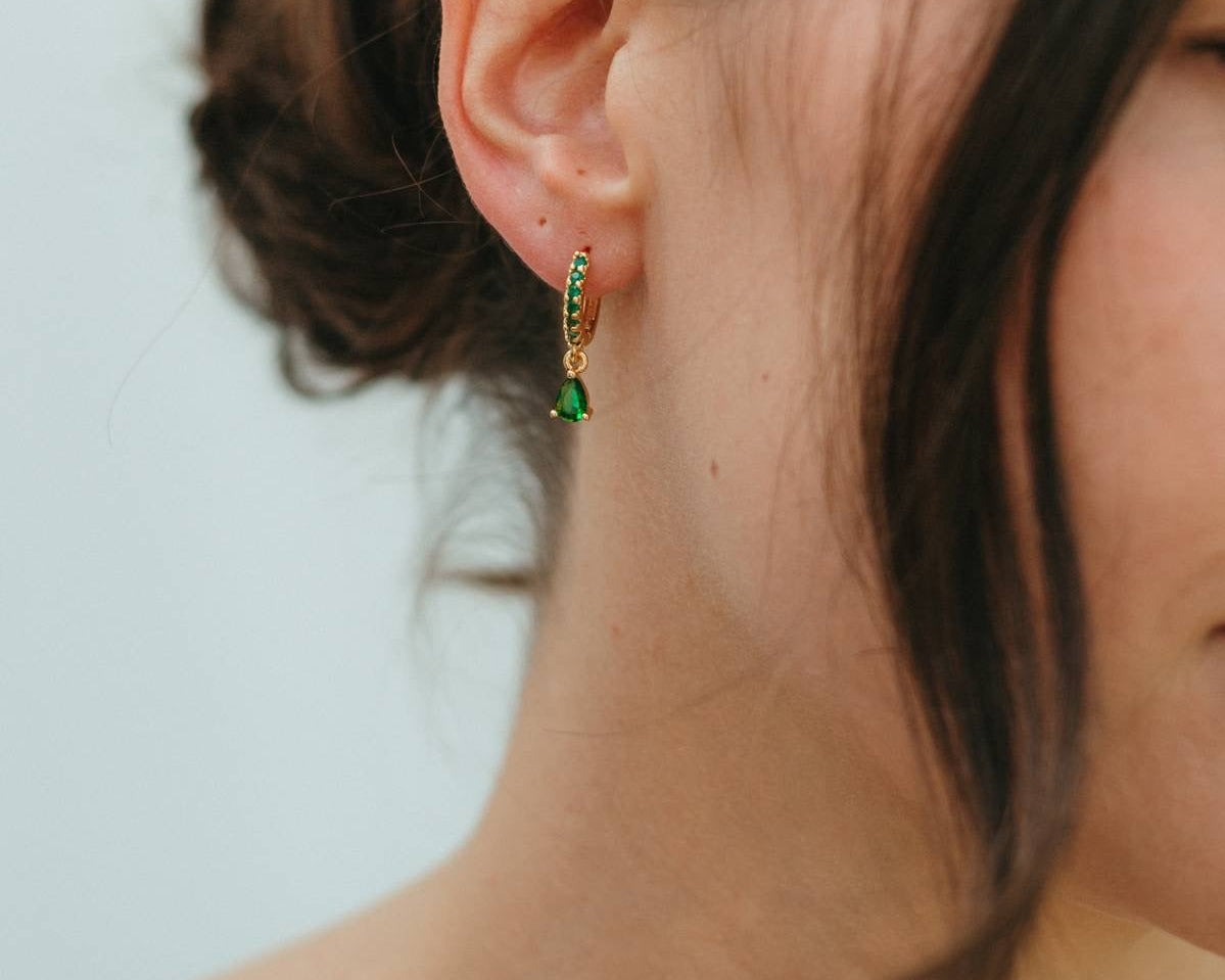 Close-up of a person wearing green earrings with a neutral background