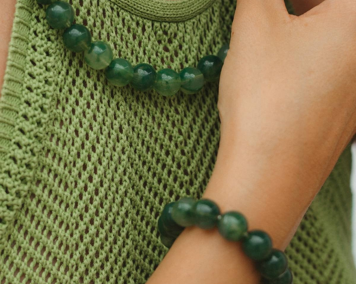 Person wearing a green beaded necklace and bracelet, close-up on green tank top.