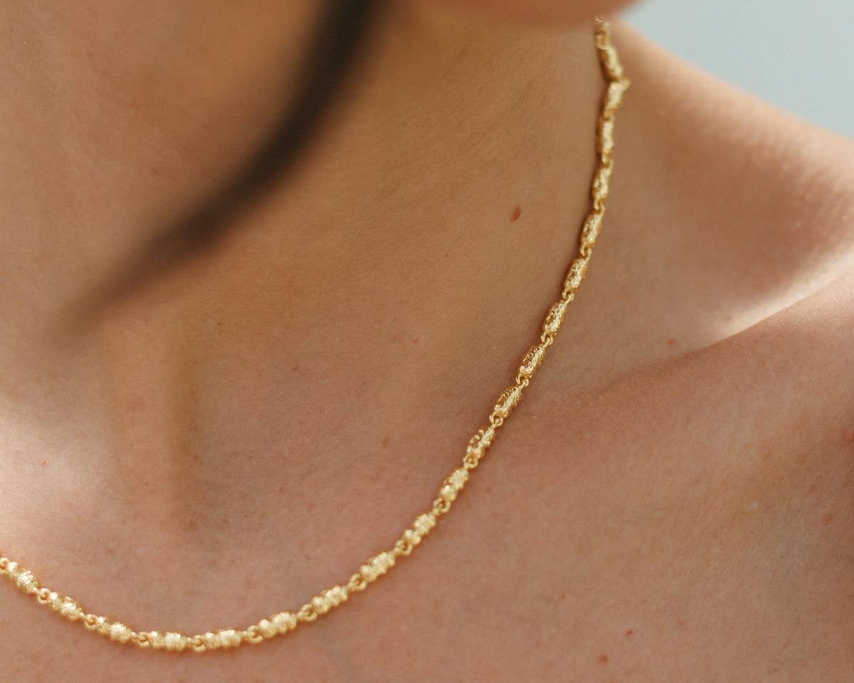 Close-up of a person wearing a gold necklace against a neutral background