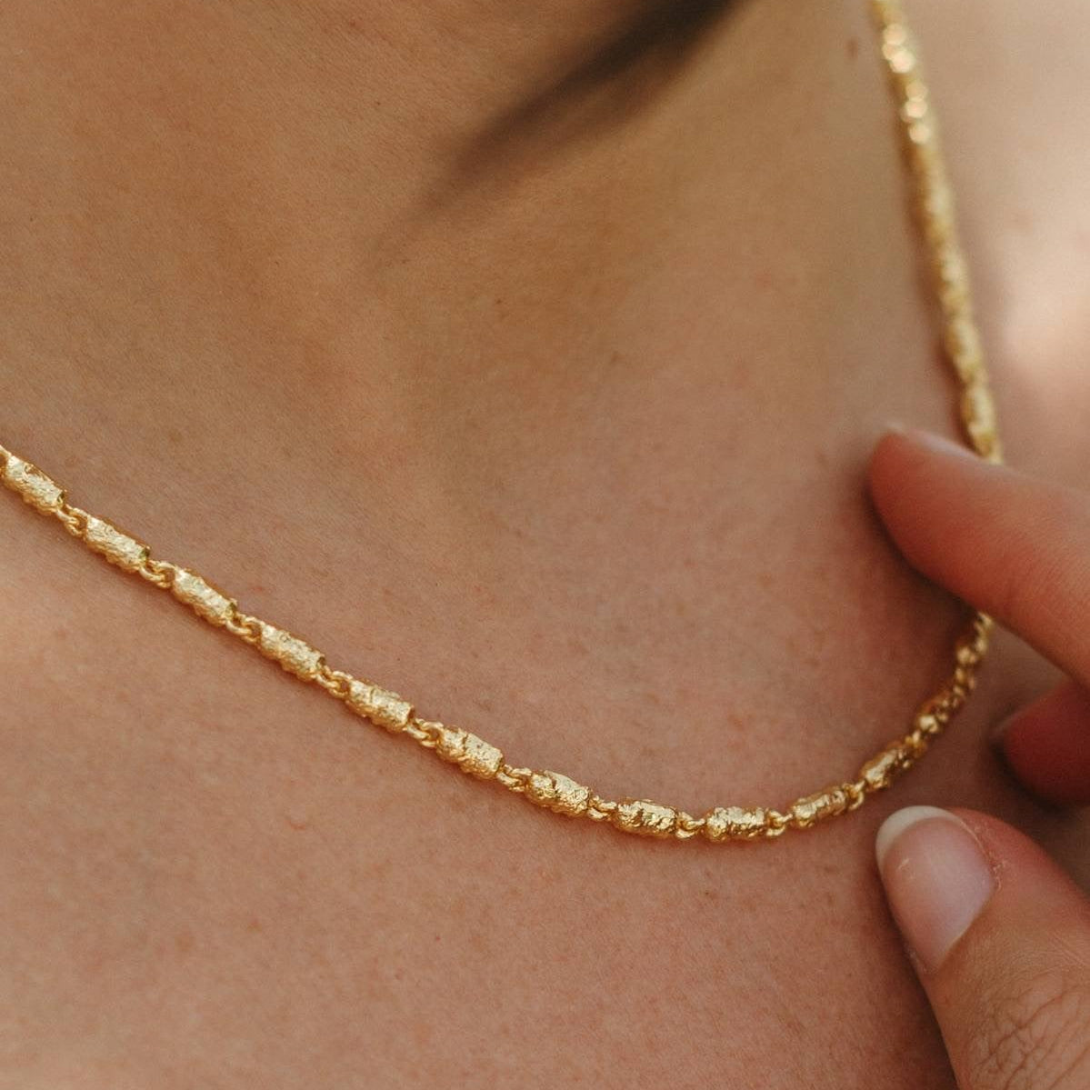 Gold necklace being worn on a person's neck with a close-up view.