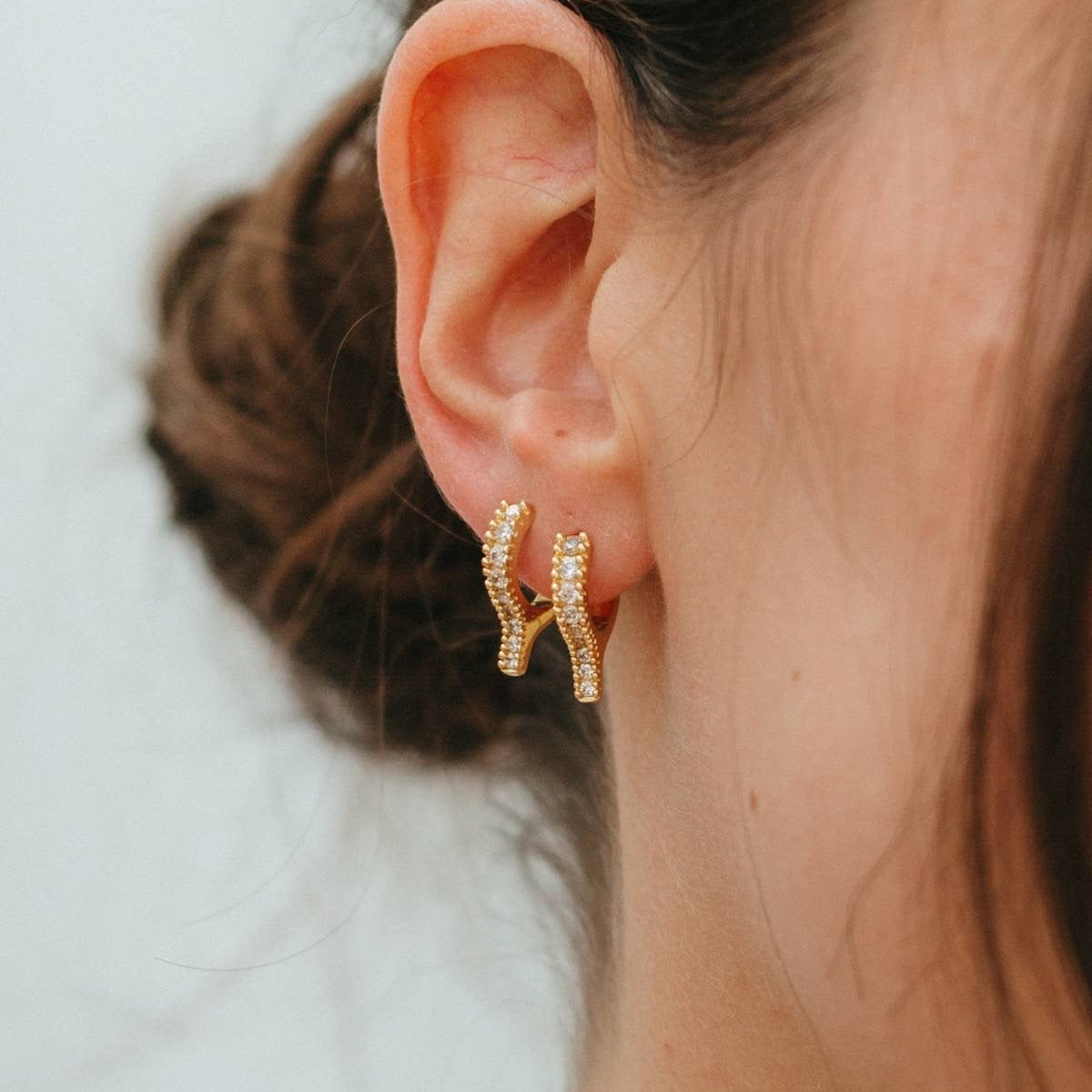 Close-up of an ear wearing gold hoop earrings with a blurred background