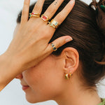 Woman wearing gold jewelry including rings and earrings against a neutral background