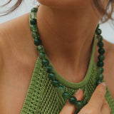 Close-up of a person wearing a green knitted top and a green beaded necklace.