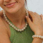 Woman wearing a green knitted top and beaded necklace with a blurred background