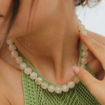 Close-up of a person wearing a green knitted top and beaded necklace.