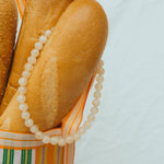 Two baguettes with a beaded necklace draped over them on a light blue background